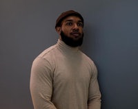 a black man in a turtleneck sweater standing in front of a wall